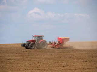 Obraz premium Tractor with a modern sowing seeds machine in a newly plowed field. Plowed land as a background. Red tractor on the field.