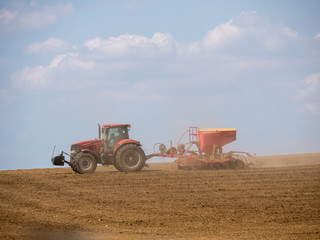 Tractor with a modern sowing seeds machine in a newly plowed field. Plowed land as a background. Red tractor on the field.
