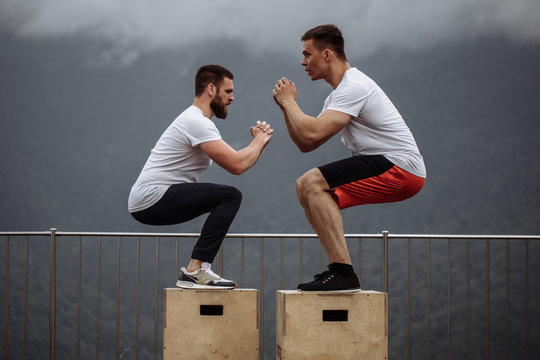 Jumping squats exercise - young handsome caucasian athletes doing functional outdoor workout in mountain area, training physical endurance and strength.