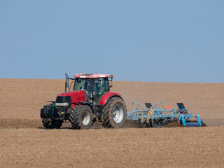 Red tractor with plow on the field. Tractor on the field. Summer field and red tractor.