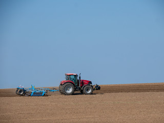 Obraz premium Red tractor with plow on the field. Tractor on the field. Summer field and red tractor.