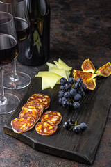 Italian antipasti wine snacks set. Cheese figs, grapes, chorizo and wine in glasses over black grunge background