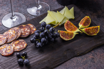 Italian antipasti wine snacks set. Cheese figs, grapes, chorizo and wine in glasses over black grunge background