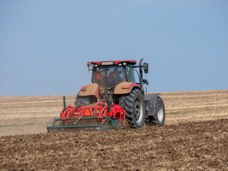 Naklejka premium Red tractor with plow on the field. Tractor on the field. Summer field and red tractor.