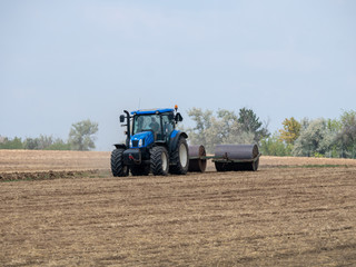 Obraz premium Tractor pulls rollers on the field. Blue Tractor with rollers on the field. Tractor on summer field.