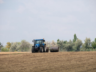 Fototapeta premium Tractor pulls rollers on the field. Blue Tractor with rollers on the field. Tractor on summer field.
