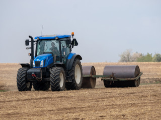 Tractor pulls rollers on the field. Blue Tractor with rollers on the field. Tractor on summer field.