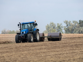 Tractor pulls rollers on the field. Blue Tractor with rollers on the field. Tractor on summer field.