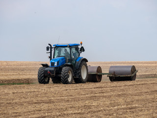 Obraz premium Tractor pulls rollers on the field. Blue Tractor with rollers on the field. Tractor on summer field.