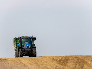 Blue tractor with trailer on the harvest field. Summer field and blue tractor with trailer. Harvest...