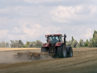 Fototapeta premium Red tractor with plow on harvest field. Summer field and red tractor. Tractor on harvest field. Lowing after harvest. Plowing on the field.