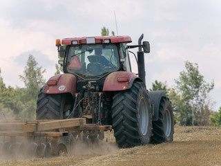 Red tractor with plow on harvest field. Summer field and red tractor. Tractor on harvest field. Lowing after harvest. Plowing on the field.