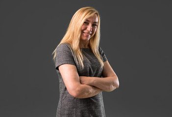 Middle age blonde woman on grey background keeping the arms crossed while smiling