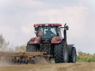 Red tractor with plow on harvest field. Summer field and red tractor. Tractor on harvest field. Lowing after harvest. Plowing on the field.