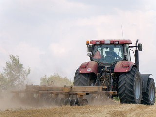 Fototapeta premium Red tractor with plow on harvest field. Summer field and red tractor. Tractor on harvest field. Lowing after harvest. Plowing on the field.