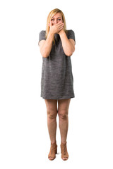 Fototapeta premium Middle age blonde woman with grey dress covering mouth with both hands for saying something inappropriate. Can not speak on isolated white background