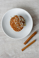 Still life morning breakfast of pancakes with honey and sprinkled with sesame seeds, cinnamon sticks on a white plate on a wooden background