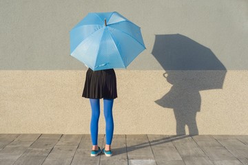 Young girl under umbrella stands with gray wall background, copy space