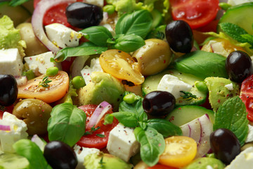 Healthy low calories salad with lettuce, heirloom tomatoes, avocado, feta cheese, red onion, cucumber, sweet peas, olives, thyme, mint and basil.
