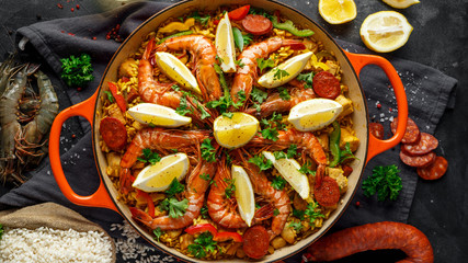 Traditional paella in the fry pan with chicken, prawns, spicy chorizo, lemon and glass of white wine.