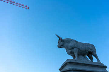 Statue eines mächtigen Stieres gegen den Himmel, in der gegenüberliegenden Ecke ein Kranausläufer