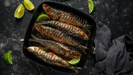 Grilled sardines with thyme, chili and lime wedges on cast iron skillet