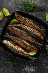 Grilled sardines with thyme, chili and lime wedges on cast iron skillet