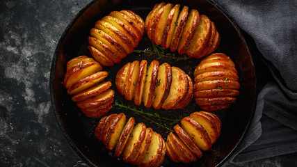 Hasselback baked potatoes served in cast-iron pan with salt, pepper and herbs