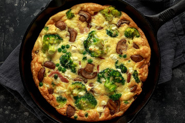 Homemade Frittata with mushrooms, broccoli, feta cheese, green peas and bacon on cast iron skillet