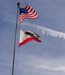 Portrait shot of the flags of the United States and the California Republic waving from one flagpole, with a streak of white clouds in the background