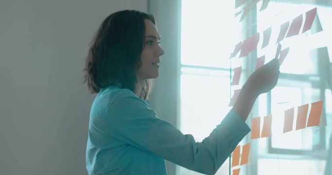 Caucasian colleagues standing near glass wall with sticky notes, framework for managing work, scrum methodology. 4K UHD 60 FPS SLOW MOTION
