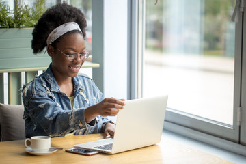 Happy satisfied African woman relaxing at cafe, enjoying morning coffee and intresting story she is reading on her laptop. People Vacations, ecreation, Holyday Concept