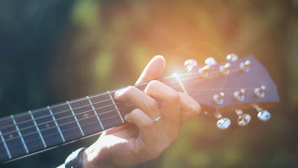 The man is playing guitar in the garden, Close-up male hand playing on acoustic guitar outdoor with bokeh and rays of sunlight.