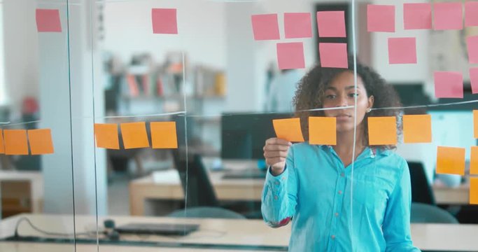 African American black employee looking onto a glass wall with sticky notes, framework for managing work, scrum methodology. 4K UHD 60 FPS SLOW MOTION