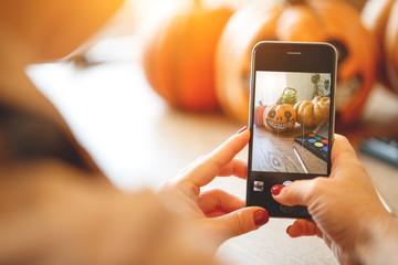 woman artist prepares for halloween and photographed on smartphone his work painted pumpkin