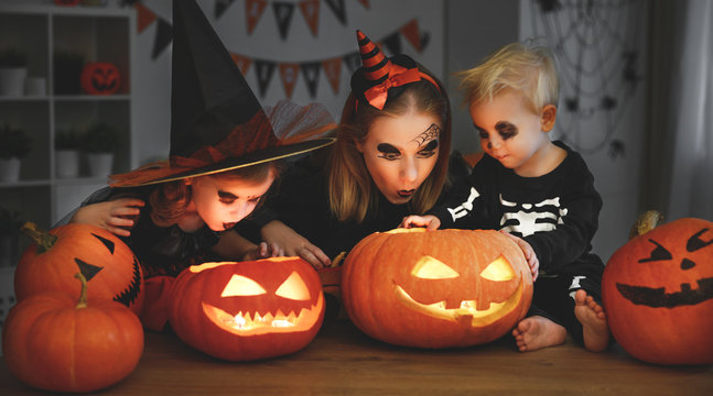 family mother and children in costumes and makeup to halloween with pumpkin in   dark