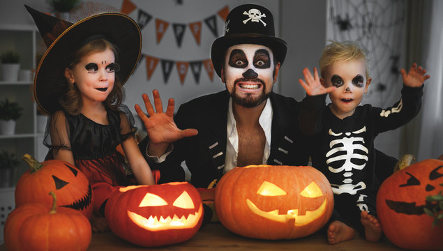 family father and children in costumes and makeup to halloween with pumpkin in   dark
