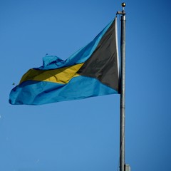 Flag of Nassau hanging from a pole with blue skies in the background