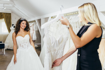 Obraz premium Beautiful young brunette woman choosing wedding dress in a bridal salon.