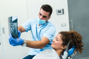 Handsome smiling dentist looking at x-ray image of his beautiful young woman patient.