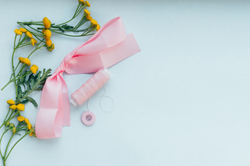 Pink thread, button, ribbon, yellow flowers on a blue background. Concept sewing. Flatlay
