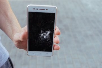 Man holds a phone with a broken screen in his hand.