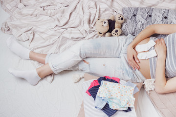 Obraz na płótnie Canvas Pregnant woman with a teddy bear and various clothes for a newborn