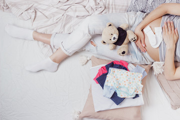 Obraz na płótnie Canvas Pregnant woman with a teddy bear and various clothes for a newborn