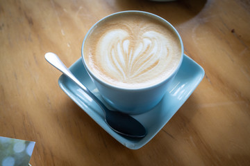Cup of coffee with latte art in heart shape on wooden table
