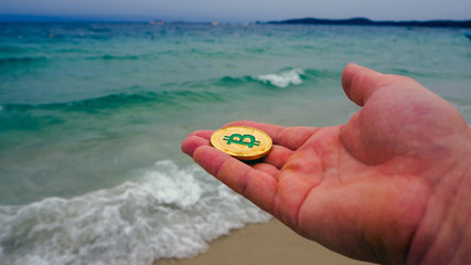 Hand holding golden bitcoin, beach