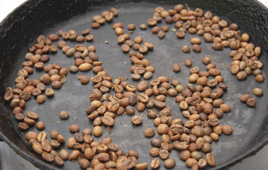 Green coffee beans roasting on the black pan