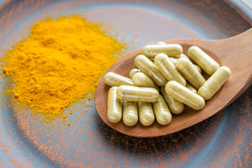 Natural herb food supplement turmeric veggie capsules and spoon with orange curcumin powder on clay plate.  Organic Turmeric extract, Curry Extract, Diferuloylmethane, JiangHuang, Curcuma Longa