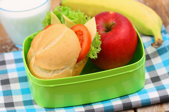 Healthy school lunchbox containing roll with cheese, lettuce and tomato, red apple and banana
