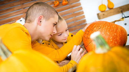 Mother and daughter drawing smiley anthropomorphic; face on a large Halloween pumpkin. Family...